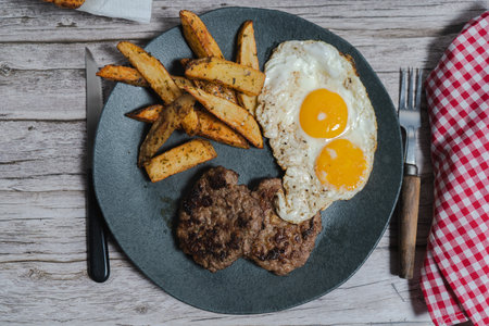 Two juicy homemade hamburgers served with fried eggs and roasted potatoes create a fulfilling and satisfying mealの写真素材