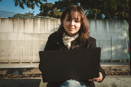 Young multitasking woman outdoors, using her notebook, modern lifestyle image.の写真素材