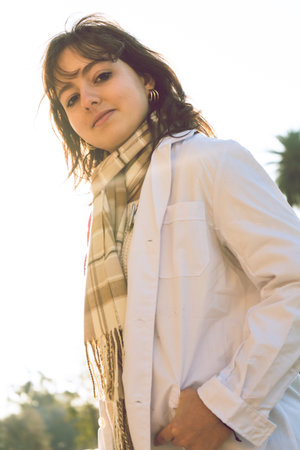 A young smiling female doctor rests outdoors, wearing her white lab coat, with the sun shining...