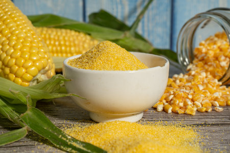 Corn flour in a bowl with fresh corn cobs and corn grits on rustic wooden table