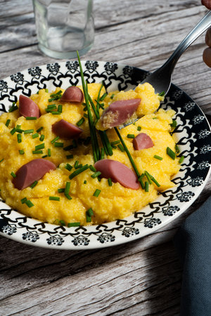 Creamy polenta with sausage and chives is being enjoyed with a fork on a rustic wooden tableの写真素材