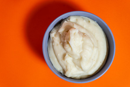 Creamy mashed potatoes served in a bowl on vibrant orange backgroundの写真素材