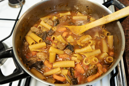 Delicious pasta with meat and vegetables is being cooked in a pot on the stove by a chef using a...