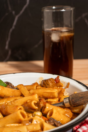 Savory beef stew served over rigatoni pasta, paired with a refreshing glass of ice-cold soda, creates a satisfying mealの写真素材