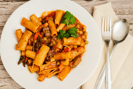 Steaming hot rigatoni pasta with beef, peas, carrots, and herbs, served on a white plate, ready to be enjoyedの写真素材