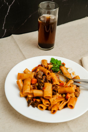 Flavorful pasta dish featuring beef, vegetables, and rich tomato sauce, served with a refreshing glass of sodaの写真素材