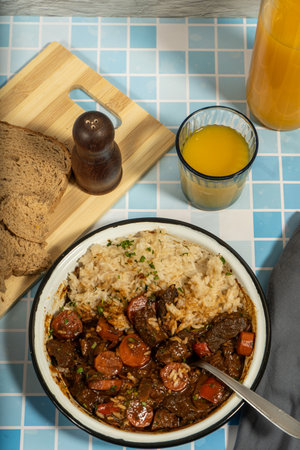 Delicious beef stew served with rice and fresh bread on a tiled tableの写真素材