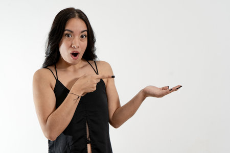 Young woman with surprised expression pointing and showing with hand on white background, ideal for advertising and marketing campaignsの写真素材