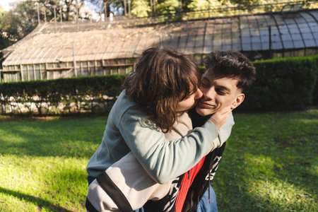 Young woman kissing her boyfriend on the cheek while piggybacking in a park