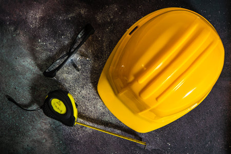 Yellow hard hat, measuring tape and safety glasses resting on dusty surfaceの写真素材