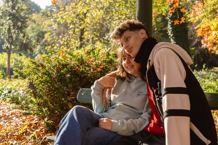 Teenagers enjoying a sunny autumn day in a park, sitting on a bench surrounded by colorful foliageの写真素材