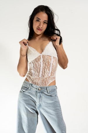 Studio portrait of a young latin woman pulling her white lace bodysuit straps while posing against a white backgroundの写真素材