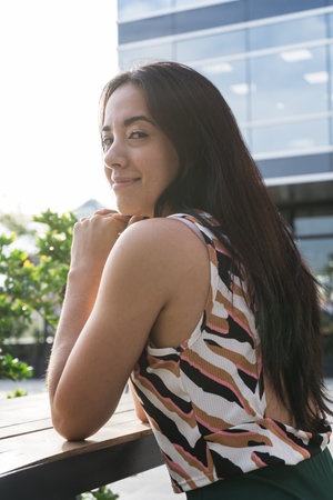 Portrait of a serene young latin woman resting her arms on a table, enjoying a moment of peace in a contemporary urban environmentの写真素材