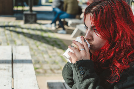 Young woman with bright red hair drinking coffee outdoors