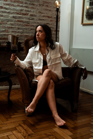Model enjoying a glass of red wine in a comfortable armchair in a stylish living roomの写真素材