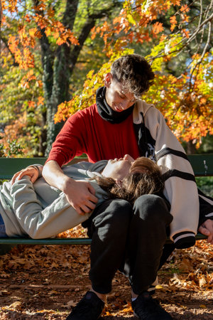 Teenagers enjoying a romantic moment together on a park bench surrounded by colorful fall foliageの写真素材