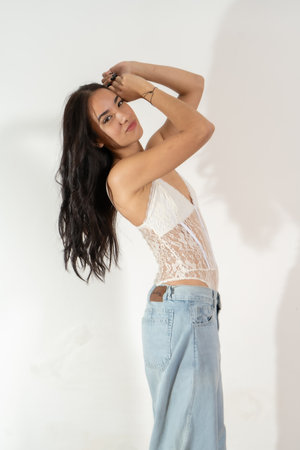 Stylish young woman poses with her hands on her head, exuding confidence and attitude against a white backgroundの写真素材