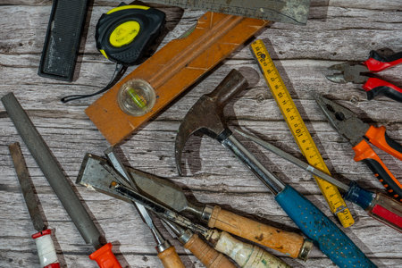 Various carpentry tools lying on wooden workbench top view showing hammer, tape measure, pliers and other toolsの写真素材