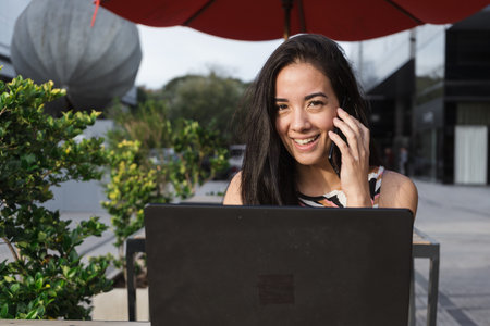 Young entrepreneur smiling and enjoying working remotely from a cafe, using her laptop and talking...