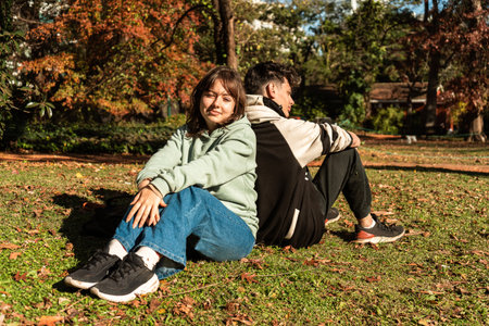 Students ignoring each other after an argument while sitting on grass in a park during autumn