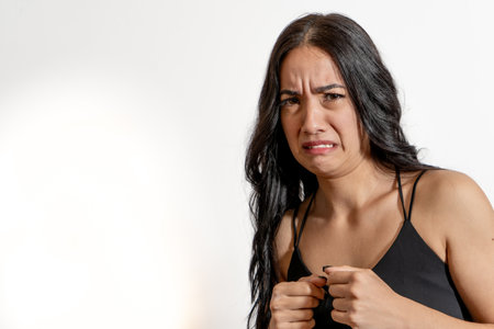Studio portrait of a young latin woman making a disgusted grimace, expressing strong dislike or...