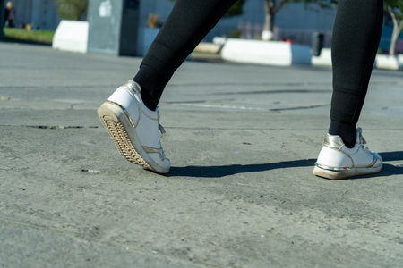 Close-up of woman's feet walking on concrete surface, wearing white sneakers and black leggings, emphasizing urban activity and footwearの写真素材