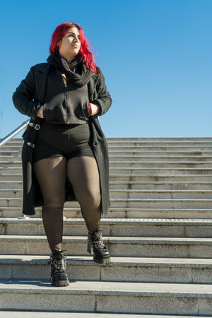 Stylish young woman with dyed pink hair and alternative clothing walking down stairs on a sunny dayの写真素材