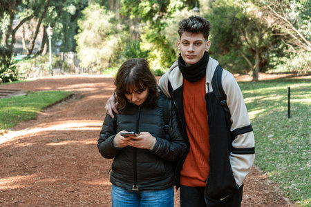 Teenage couple walks in a park while using a smartphone and enjoying each other's companyの写真素材