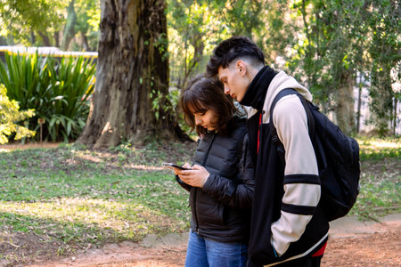 Two students are using a smartphone in a park, enjoying nature and technologyの写真素材