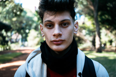 Portrait of a stylish young man wearing a black neck warmer and hoodie in a parkの写真素材