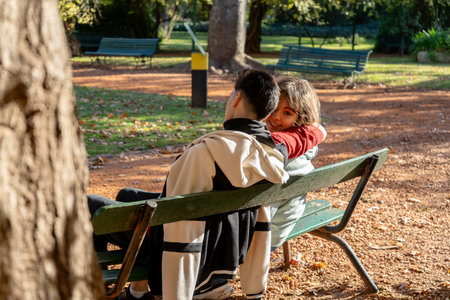 Romantic couple cuddling on a bench in a park, enjoying the warm autumn sunlightの写真素材