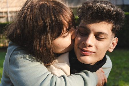 Romantic couple sharing a tender moment outdoors, embracing and kissing on the cheekの写真素材
