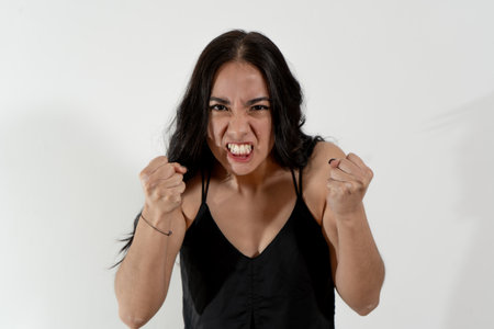Studio portrait of a young latin woman expressing anger and frustration with clenched fistsの写真素材