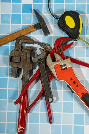 Claw hammer, pliers, wrenches and measuring tape lying on blue bathroom tiles, ready for renovation workの写真素材
