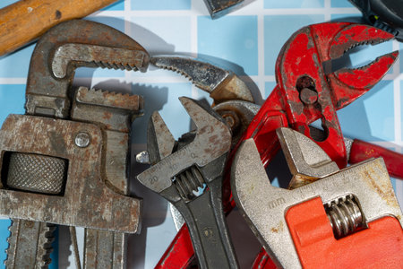 Many well-used wrenches and pipe wrench are laying on blue tiles, showing signs of wear and tearの写真素材