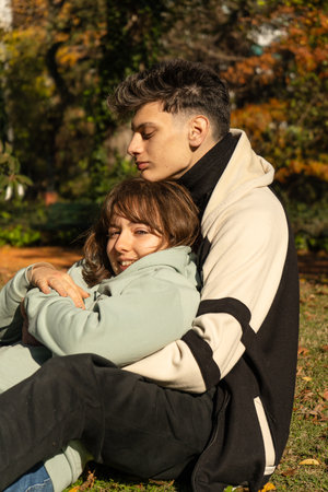 Young couple cuddling on grass in autumn park, enjoying a romantic moment togetherの写真素材