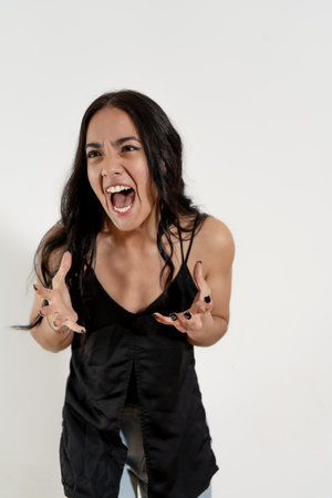 Angry hispanic woman screaming with open mouth and gesturing with hands on white backgroundの写真素材