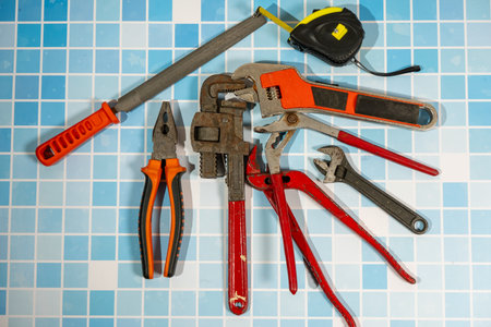 Different plumbing tools lying on blue bathroom tiles ready for a home improvement and repairing...