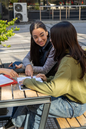 Two female university students are working together on a project at an outdoor table, sharing ideas...