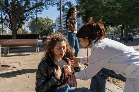 Female doctor examining a young woman on a city street, using a stethoscope to check her heartbeatの写真素材