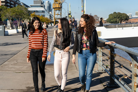 Three friends enjoying a sunny day in Puerto Madero, Buenos Aires, walking along the river and chattingの写真素材