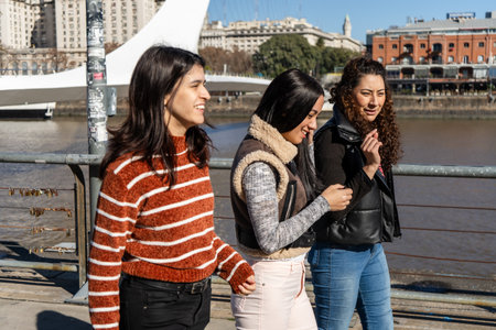 Three young women enjoy a sunny day, chatting and laughing together by the river in the Puerto...