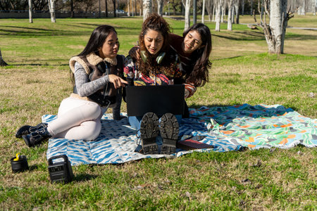 Three students collaborating on a laptop in a sunny park, enjoying fresh air and teamworkの写真素材