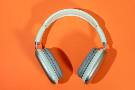Stylish light green wireless headphones on a vibrant orange background, representing music, technology, and audio enjoymentの写真素材