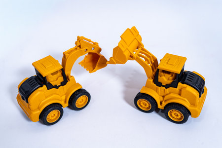 Two yellow toy excavators facing each other on white backgroundの写真素材