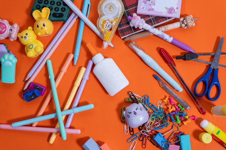 Colorful school supplies arranged on vibrant orange background for back to school seasonの写真素材