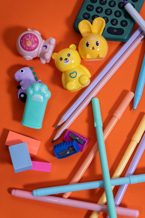 Colorful pencils, pens, erasers, sharpeners, and fun pencil sharpeners are arranged on a vibrant orange surface, ready for the back-to-school seasonの写真素材
