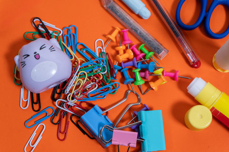 Colorful stationery items creating a vibrant and disorganized arrangement on an orange backdrop