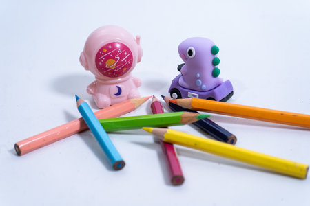 School supplies including colored pencils, a dinosaur eraser and an astronaut pencil sharpener rest on a white surface, ready for creative endeavorsの写真素材