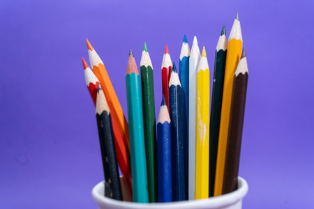 Colorful pencils standing in a white cup on a purple background, ready for creative endeavorsの写真素材